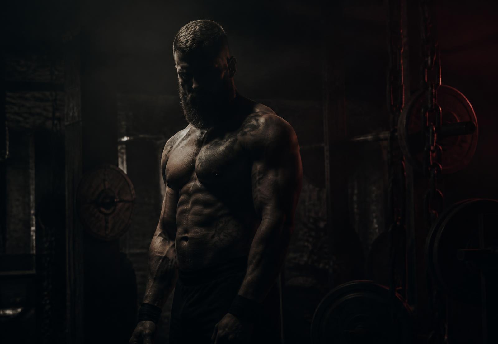 Competitive bodybuilder standing in shadow in a dark iron gym